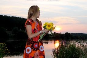 girl with sunflowers near the water at sunset