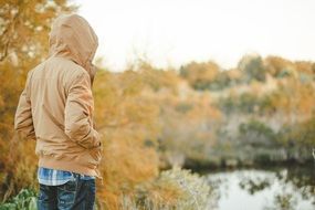 young man in a beige jacket on the lake shore view from the back