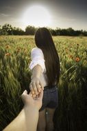 Girl holding male hand walks in field at Sunset