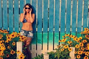 beautiful girl in a bikini near a fence among sunflowers