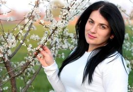 the girl stands near a tree with white leaves
