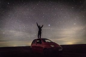 man is standing on a red car at night