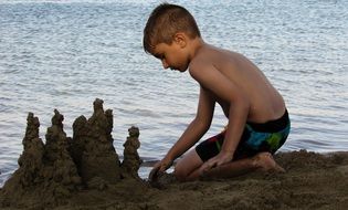 Child Boy builds sand castle on beach