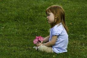 little girl with a pink bouquet sits on green grass