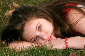 girl with blue eyes lies on green grass