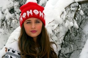 Girl in a red hat near a tree in the snow