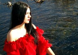 girl in a red dress sits near the water