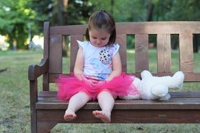 Girl with a toy in the form of a teddy bear on a bench