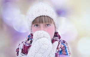 Girl in a knitted cap and mittens in the glare of light