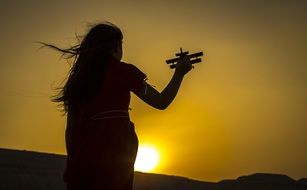 silhouette of a girl with an airplane in hands at sunset