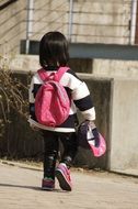 A small child with a pink backpack is walking along the road