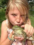 Blonde girl is kissing green frog