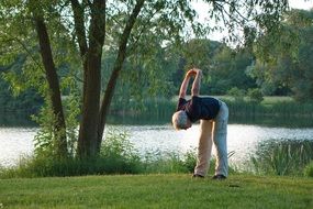 sporty man does exercises on the river bank