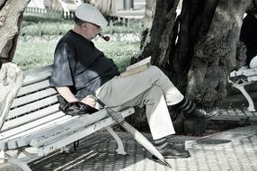 an elderly man smoking and reading in the Park