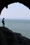 photo of a man on a rock through a cave