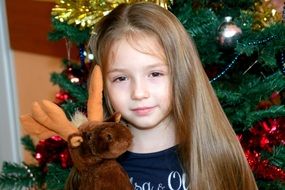 little girl with a soft deer near the Christmas tree