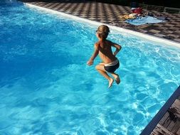 Child boy jumping in blue swimming pool in light