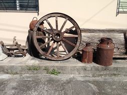 old wooden wheel and pots at wall