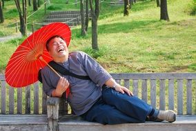 a man with a red umbrella lies on a bench