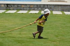 boy pulls a rope on a green field