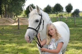 cute blonde girl stand near white horse