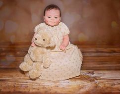 baby doll in a beige dress with teddy bear