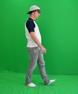 barefeet man in grey jeans and cap walking at green background