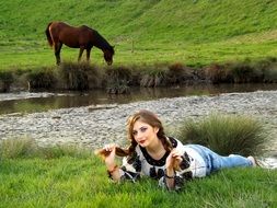 young Girl lays down on meadow in front of water