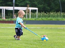 little boy carrying a toy on the green grass