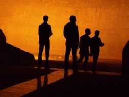 four silhouettes of men on a background of an orange wall