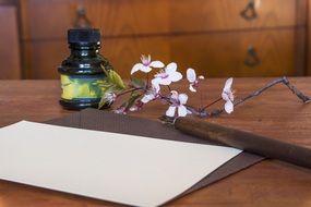 empty sheet of paper, pen, cherry blossom and bottle on table