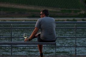 man with a wine glass in his hands resting on a wooden bench