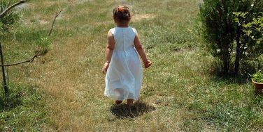 girl in a white dress walks on the green grass