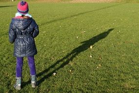 little girl stands on green grass with shadow