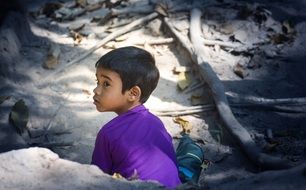 photo of child sits behind a stone in a purple t-shirt