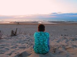 young man in a green T-shirt sitting on the beach view from the back