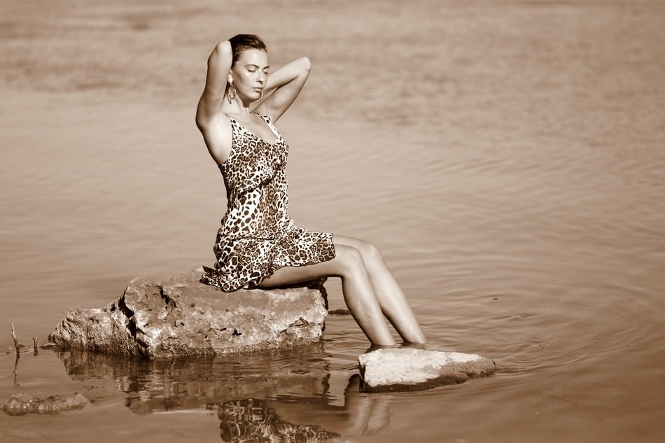 brunette in a leopard dress on a stone in the water in monochrome background