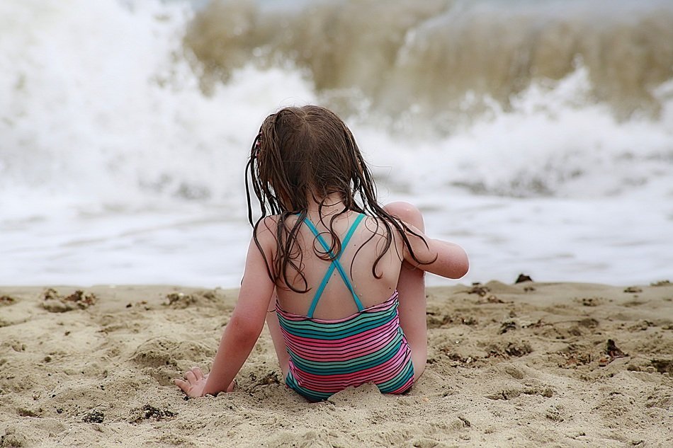 Child girl with wet hair sits on beach at Waves