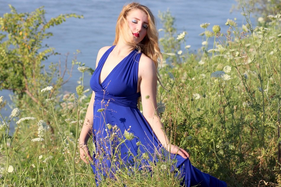 blonde in a blue dress in tall grass near the water