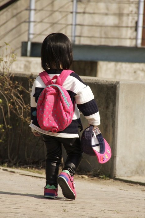 A small child with a pink backpack is walking along the road
