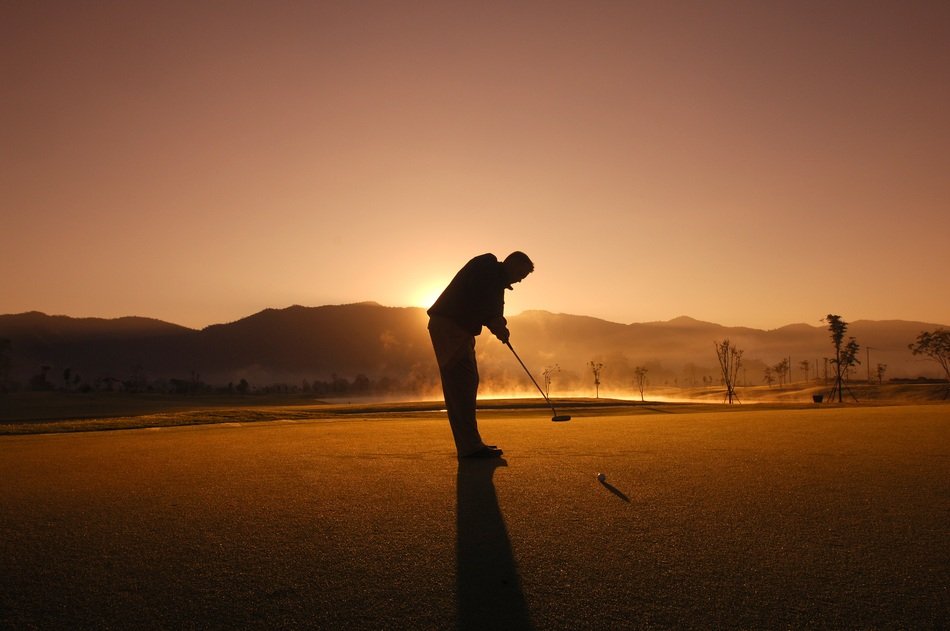 silhouette of a man on a golf course at sunset