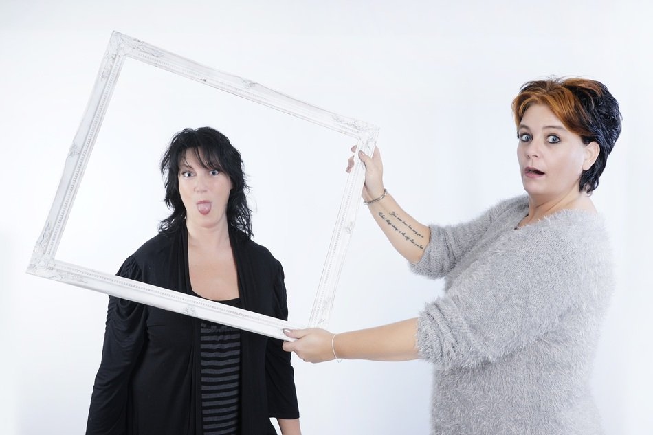 young woman holding frame in front of girl with stick out tongue
