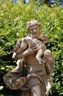 Baroque sculpture at greenery, old man with child boy across shoulder