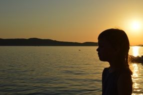 silhouette of a little girl near the lake at sunset