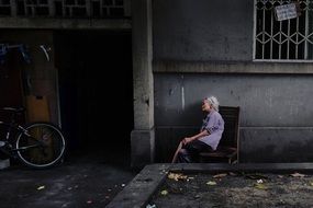 elderly woman on a chair in the street at the entrance to a house in China