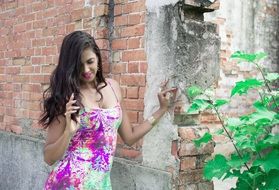 model in a colorful dress against a brick wall near the plants