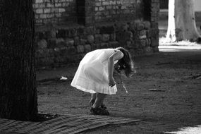 Child Girl in White Dress with key on neck correcting her shoe