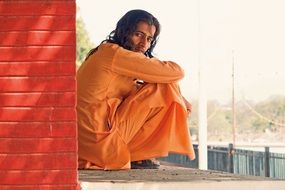 indian male model in orange suit sitting against a brick wall