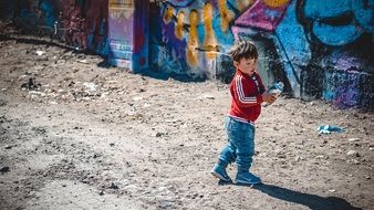 little boy stands near the wall with graffiti