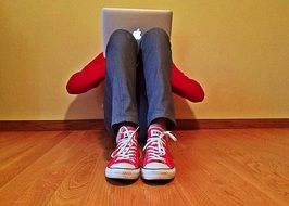 young man with laptop on wooden floor in room